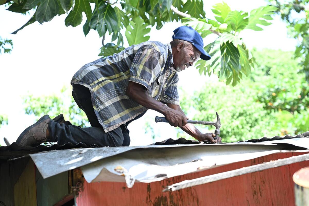 Un hombre protege el techo de su casa con laminas de zinc ante la inminente llegada del huracán Beryl este martes en Saint Thomas (Jamaica). | EFE/Rudolph Brown
